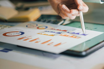 Photo of a report with infographics, a laptop, and a man holding a pen
